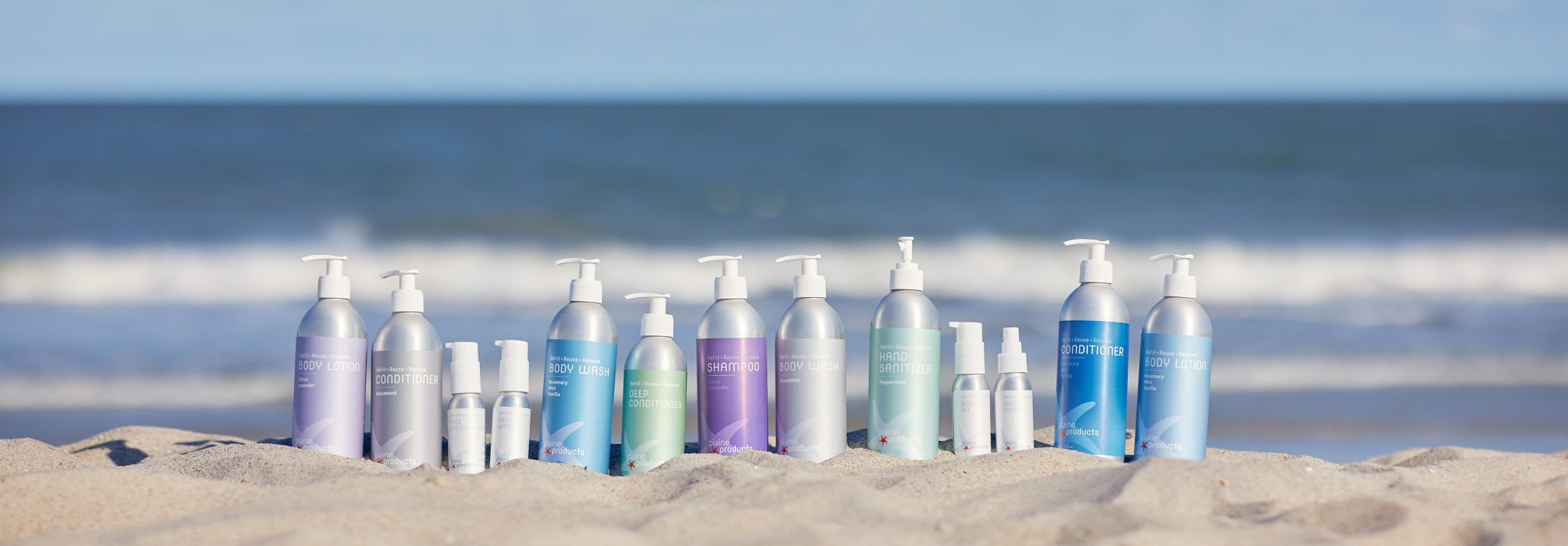 Plaine Products refillable aluminum hair and skin care bottles on a beach, because they reduce plastic pollution